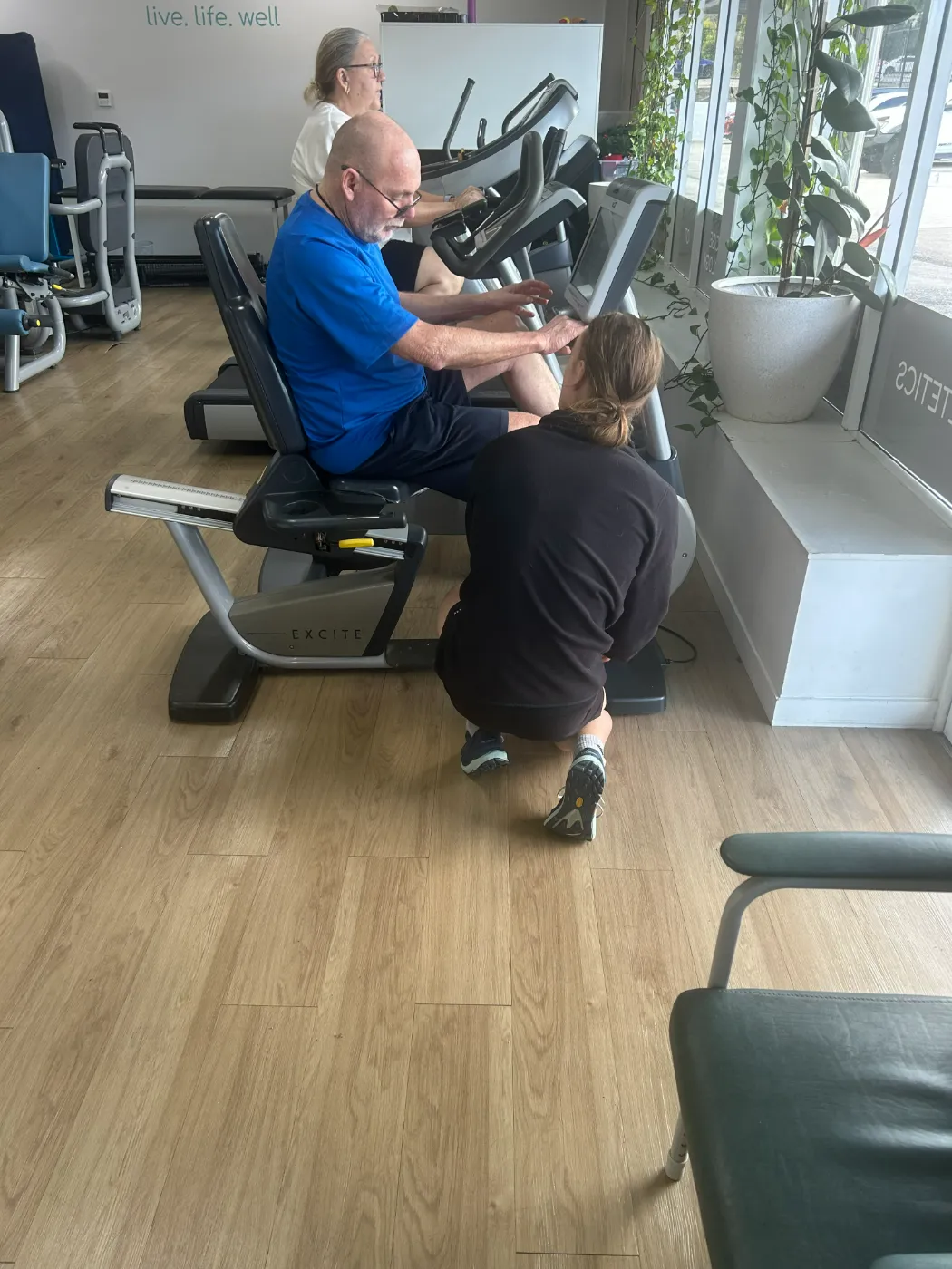 A participant exercising on accessible gym equipment with support nearby