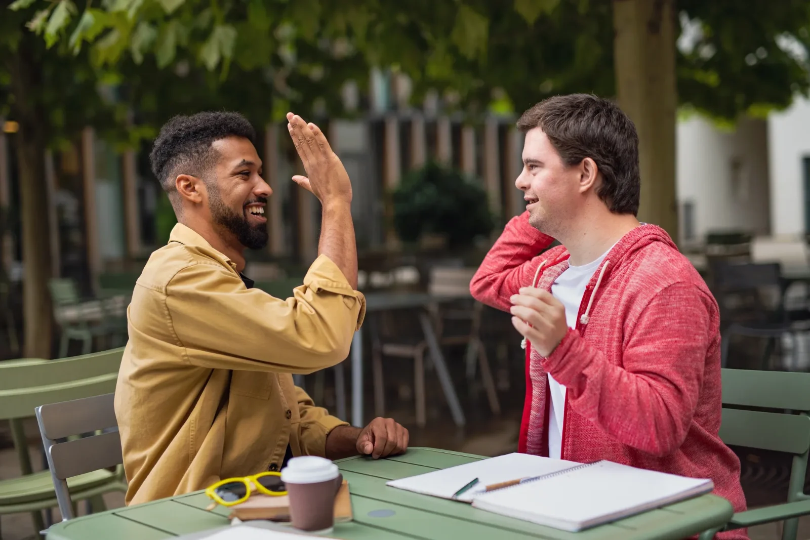 Two friends sharing a high-five at an outdoor café table